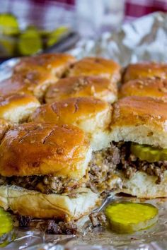 a close up of a sandwich on tin foil with pickles in the foreground