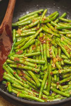 cooked green beans in a frying pan with a wooden spoon next to it and sauce on the side