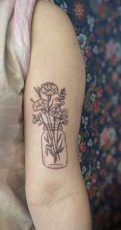 a woman's arm with flowers in a jar tattoo on the left upper arm