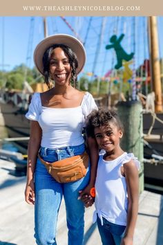 a woman standing next to a little boy on a dock wearing a hat and jeans