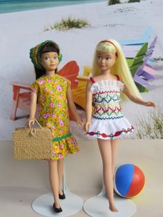 two dolls standing next to each other near a beach ball and palm tree in the background