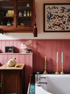 a bath tub sitting next to a wooden cabinet with candles on top of it in a bathroom