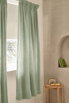 a green curtain hanging from a window next to a small table with a clock on it