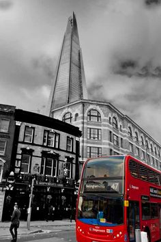 a red double decker bus driving down a street in front of a tall building with a steeple