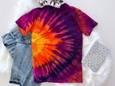 a tie - dyed shirt and denim shorts are laid out on a white fur rug