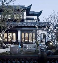 an outdoor living area with couches and tables in front of a large house at night