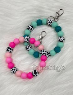 two bracelets with pink, blue and green beads are on a white fur surface