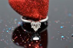 a heart shaped diamond ring sitting on top of a table next to a red glittered object