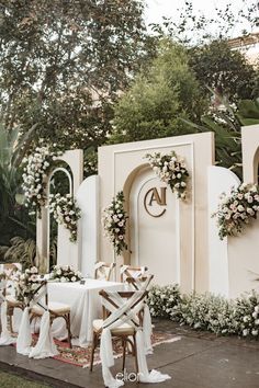 an outdoor wedding setup with white flowers and greenery on the walls, chairs and tables