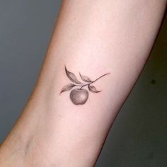 a small apple tattoo on the left inner arm, with two leaves and an apple on it