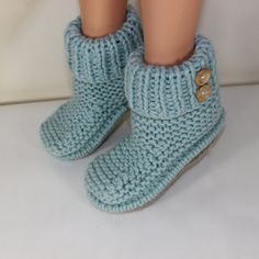 the legs of a doll wearing blue knitted slippers with buttons on them, standing in front of a white background