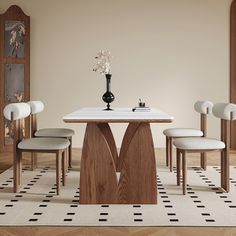 a dining room table with four chairs and a vase on top of it, in front of a beige wall