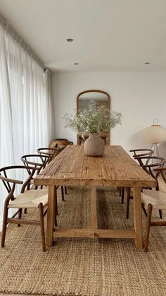 a dining room table with chairs and a vase on top of it in front of a window