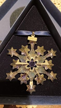 a gold and black snowflake is on display in a glass case with a ribbon around it