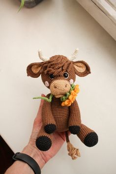 a hand holding a small stuffed animal with horns and flowers on it's neck