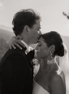 a bride and groom kissing each other outside