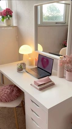 a laptop computer sitting on top of a white desk next to a pink flower pot