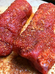 two pieces of meat sitting on top of a wooden cutting board covered in seasoning