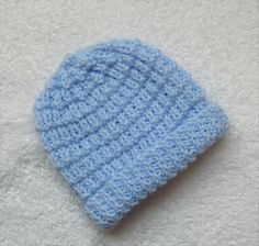 a blue crocheted hat laying on top of a white blanket