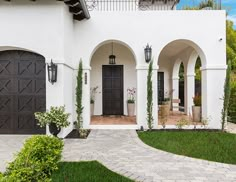 a white house with two black doors and some green plants in the front yard area