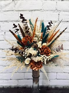 a vase filled with flowers and feathers on top of a wooden table next to a brick wall