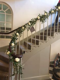 white roses and greenery are on the handrail of a stair case in a house