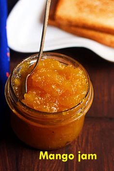 a spoon in a jar filled with mango jam on top of a table next to toast