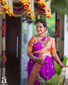 a woman in a purple and orange sari is standing under an archway with flowers