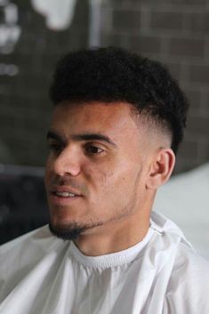 a close up of a person wearing a white shirt and black hair with a brick wall in the background