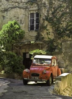 an old red car parked in front of a stone building with ivy growing on it