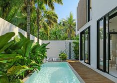 an outdoor swimming pool surrounded by greenery and palm trees in front of a house