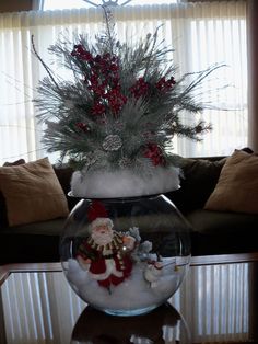 a christmas decoration in a fish bowl on a table with a couch and window behind it