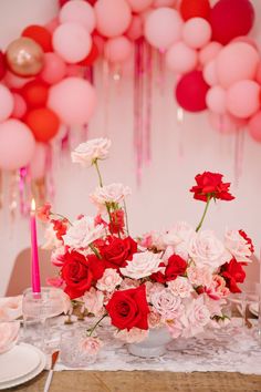 the table is set with pink and red flowers, candles, and balloons in the background