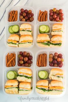 several plastic containers filled with sandwiches, crackers and grapes next to cucumbers