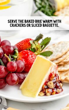 a white plate topped with crackers covered in cheese next to grapes and strawberries