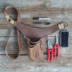 a leather tool pouch with some tools in it on top of a wooden table next to a cell phone