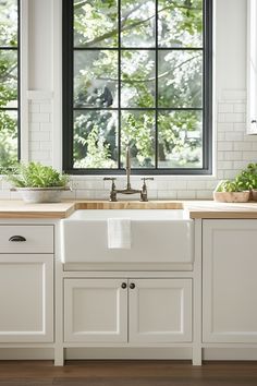 a white kitchen with black windows and wooden counter tops, along with potted plants on the window sill