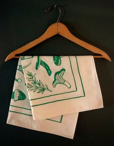 two white and green napkins hanging on a wooden hanger next to a black wall