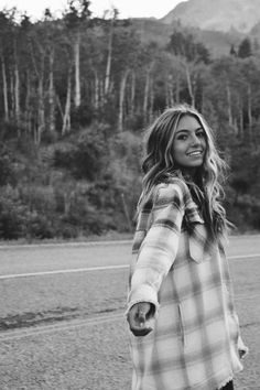 a woman riding a skateboard down the middle of a road with trees in the background