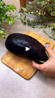 a person holding an eggplant on top of a cutting board next to plants