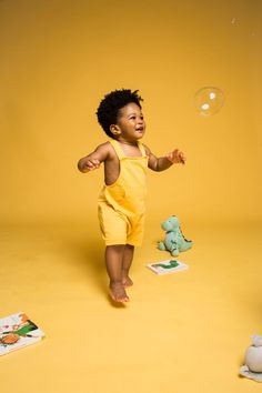 a small child in yellow jumpsuits playing with soap bubbles on a yellow background