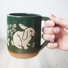 a hand holding a green coffee mug with a white rabbit on it