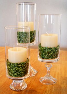 three clear glass vases filled with green moss and lit candles on a wooden table