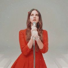 a woman in red dress holding a microphone with snow falling on the ground behind her