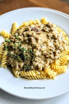 a white plate topped with pasta covered in mushroom gravy and garnished with herbs