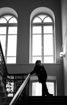 black and white photograph of a man walking down the stairs in front of two windows