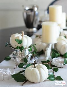 white pumpkins and greenery on a table with candles in the middle, along with other decorations