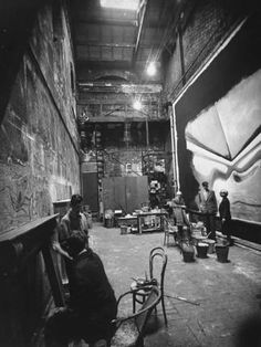 an old black and white photo of people working in a factory with large paintings on the walls