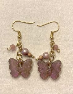 two pink butterflies with pearls and beads on gold earwires are hanging from brass hooks