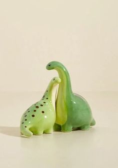 two ceramic dinosaurs sitting next to each other on a white surface with a light colored background